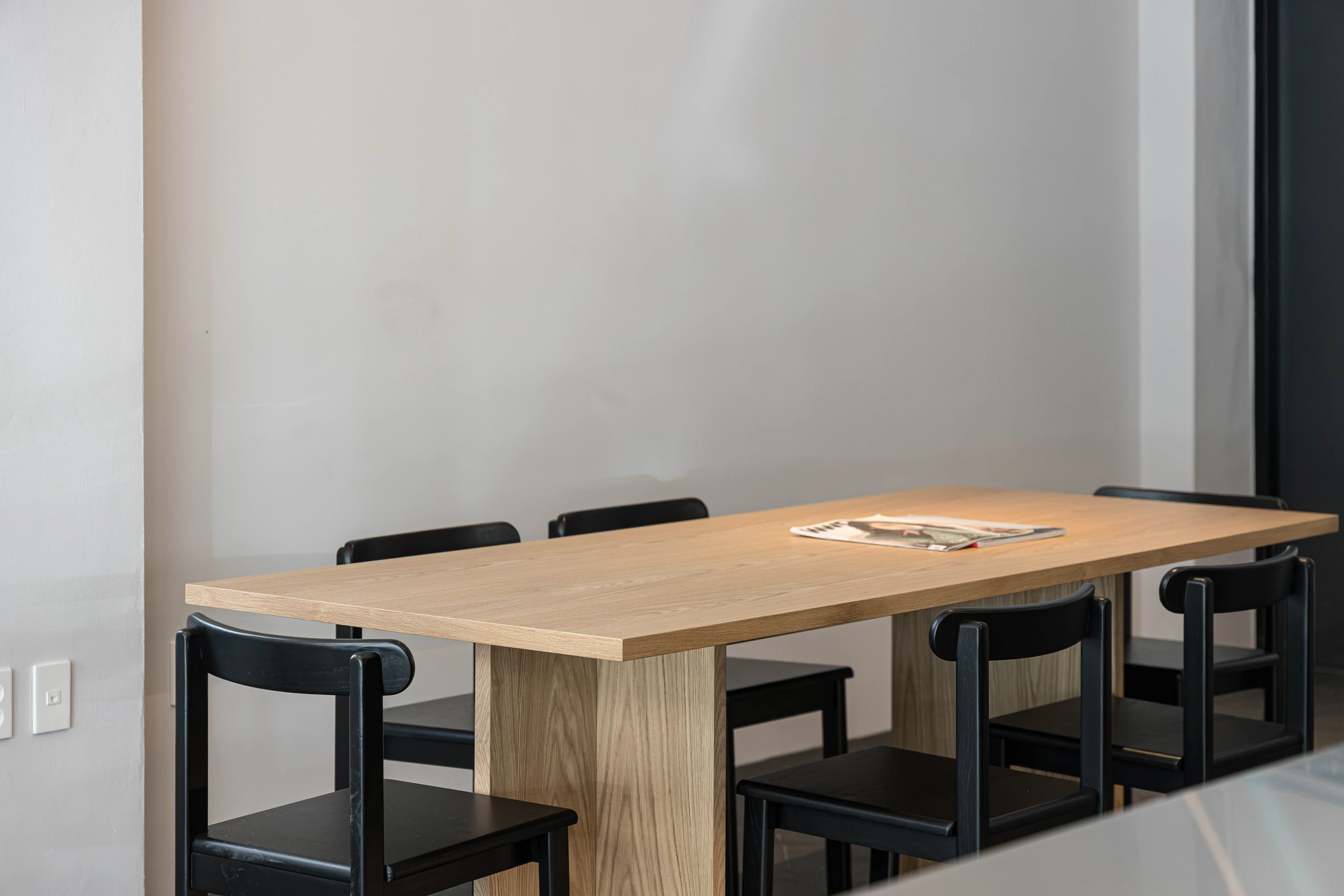 Communal timber table and black chairs beside the cafe window
